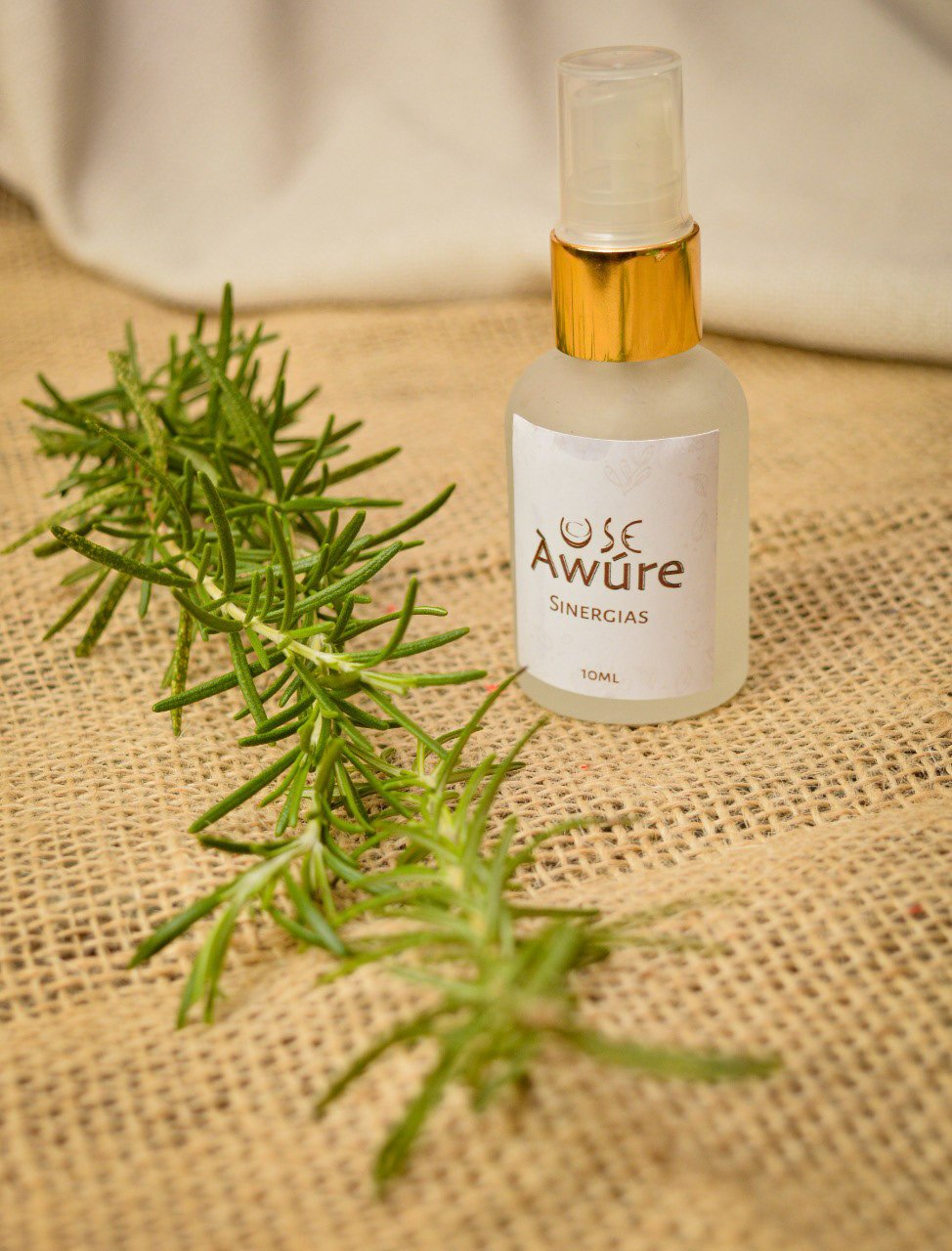 USE Àwúre Sinergias spray bottle photographed with fresh rosemary on jute fabric